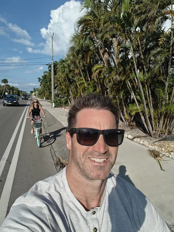 Cyclists enjoying a sunny afternoon ride on a paved path lined with lush palm trees under a bright blue sky.